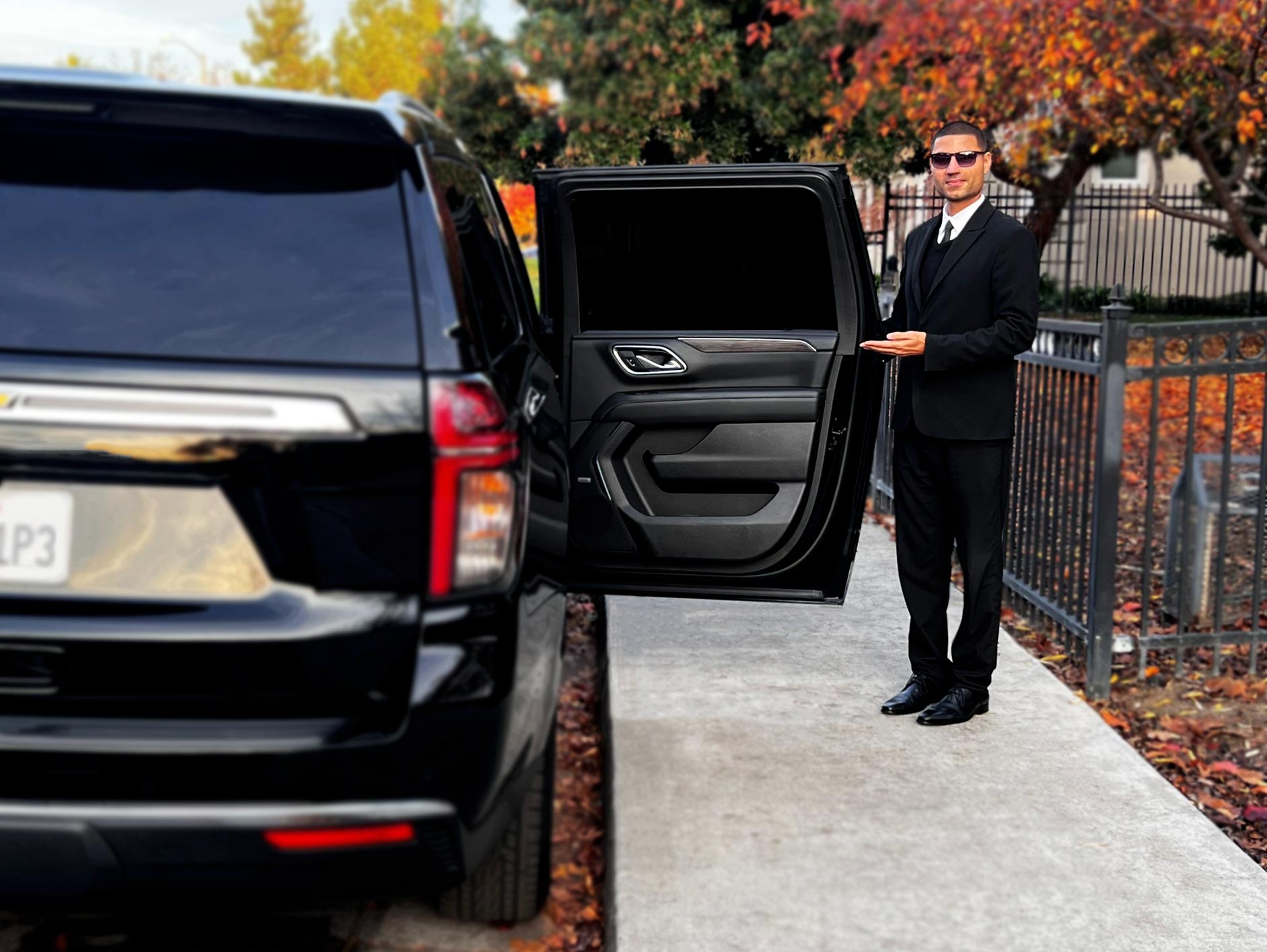 Professional driver in a suit opening the door of a luxury SUV for a customer