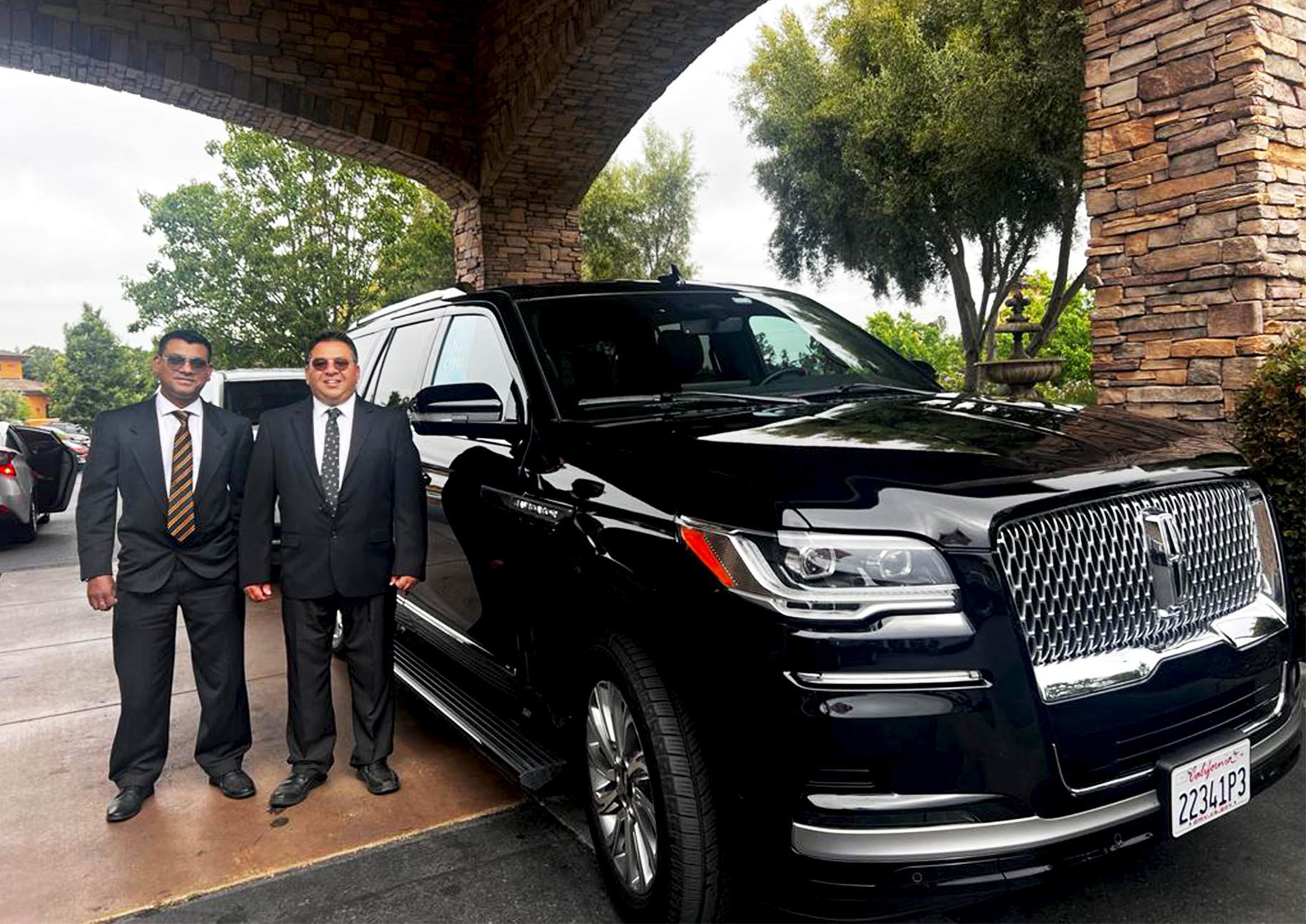 Professional chauffeurs standing beside a luxury black SUV, ready to provide premium transportation services from Prunedale.