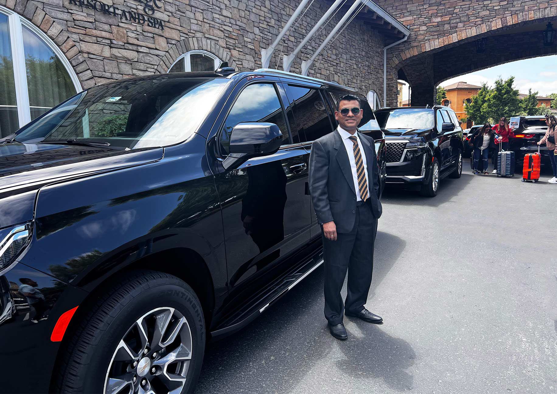 Professional chauffeur standing beside a luxury SUV, providing exceptional transportation services at a high-end location.